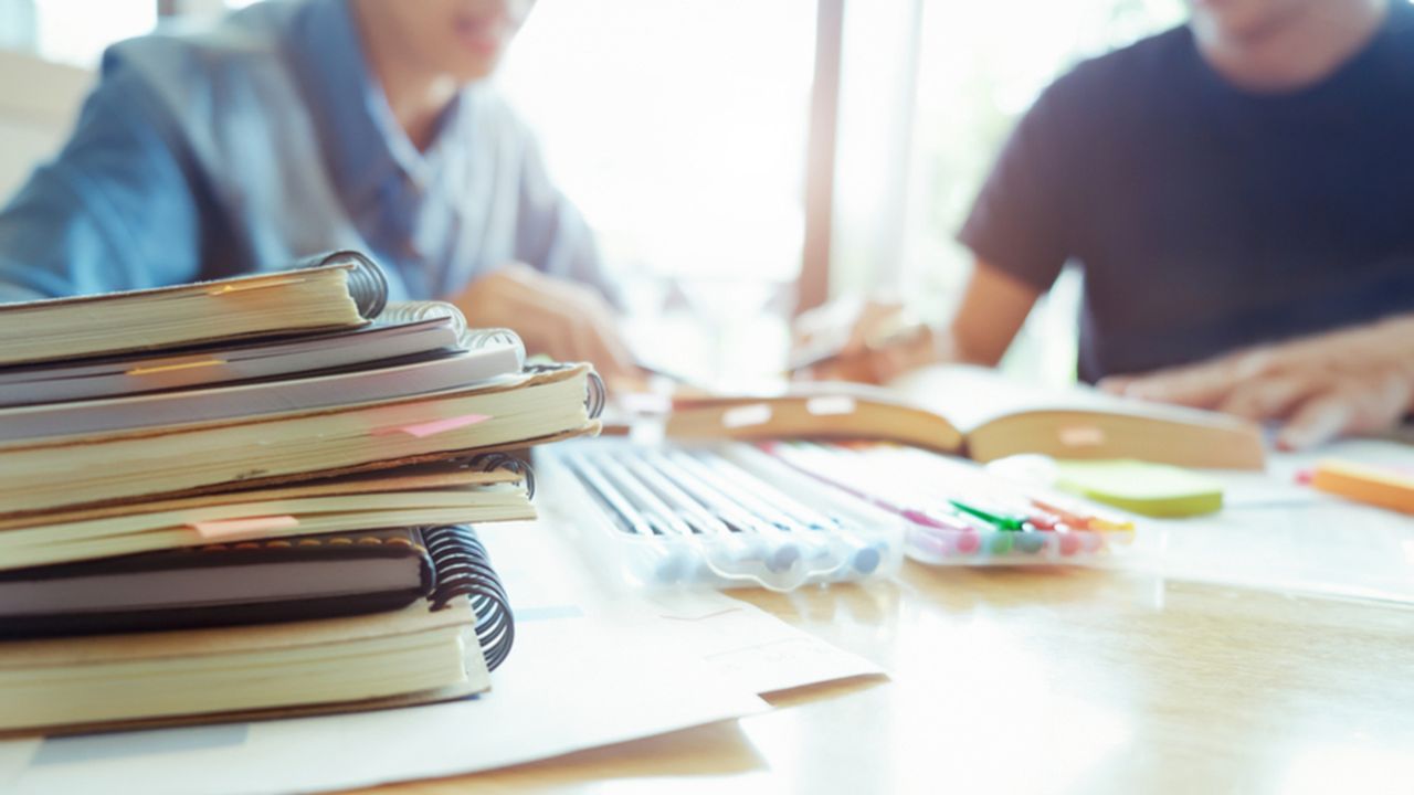 Livre au premier plan avec deux personnes suivant un cours
